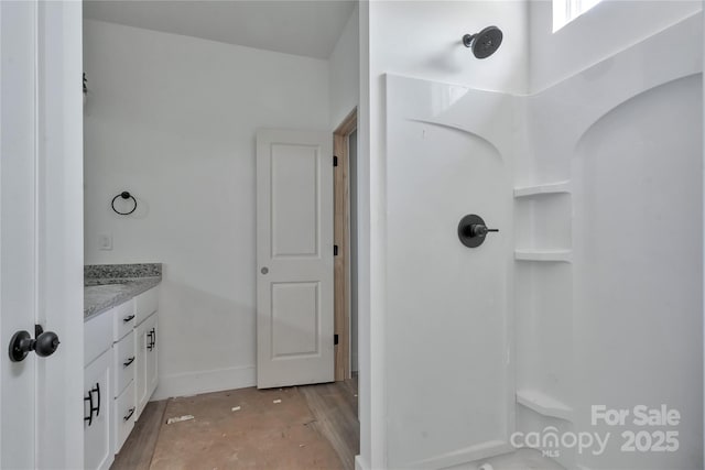 bathroom featuring walk in shower, baseboards, and vanity