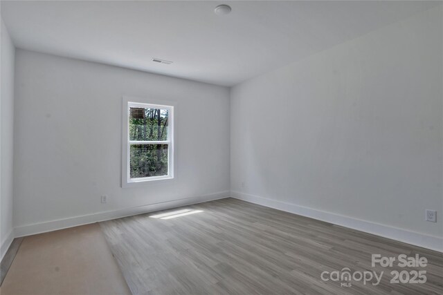 empty room featuring wood finished floors, visible vents, and baseboards