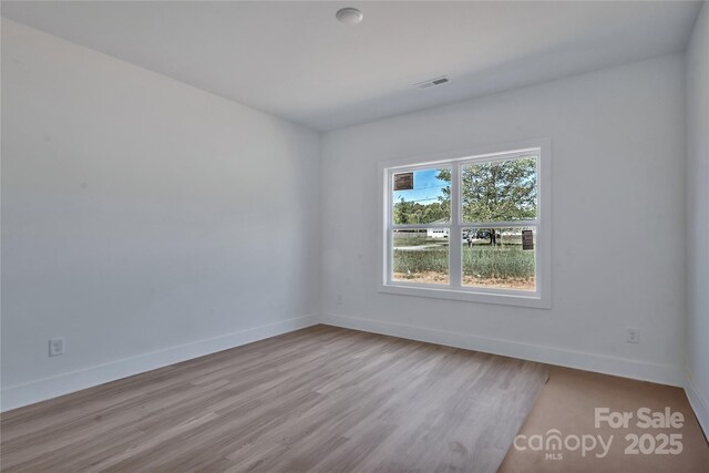 unfurnished room featuring wood finished floors, visible vents, and baseboards