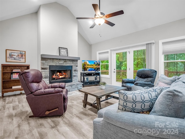 living room featuring a stone fireplace, ceiling fan, light hardwood / wood-style floors, and high vaulted ceiling