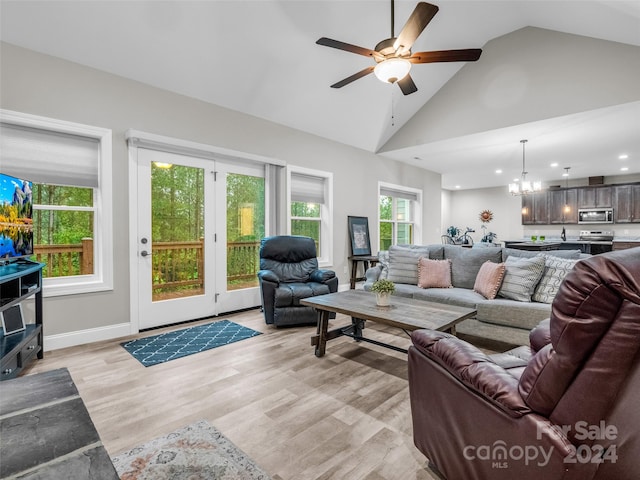 living room with high vaulted ceiling, a wealth of natural light, ceiling fan with notable chandelier, and light hardwood / wood-style flooring