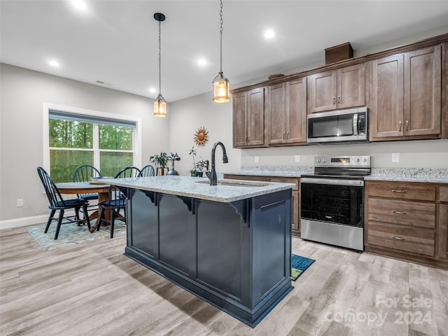 kitchen with hanging light fixtures, light wood-type flooring, stainless steel appliances, light stone counters, and sink