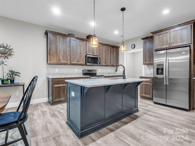 kitchen with light hardwood / wood-style floors, pendant lighting, sink, a kitchen bar, and appliances with stainless steel finishes