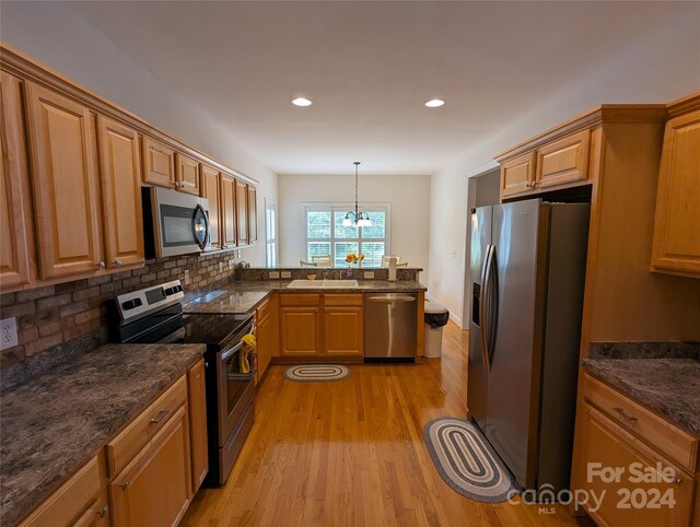 kitchen with light wood-type flooring, stainless steel appliances, dark stone counters, decorative light fixtures, and backsplash