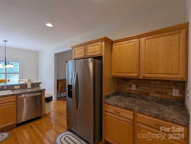 kitchen with dark stone counters, light hardwood / wood-style flooring, an inviting chandelier, hanging light fixtures, and appliances with stainless steel finishes