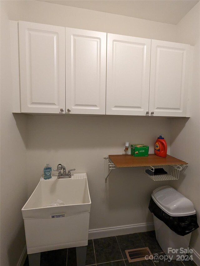 laundry area featuring sink and dark tile flooring