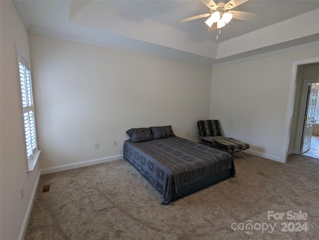 carpeted bedroom with a tray ceiling, ornamental molding, and ceiling fan