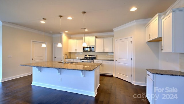 kitchen featuring hanging light fixtures, dark stone countertops, a center island with sink, appliances with stainless steel finishes, and dark hardwood / wood-style floors