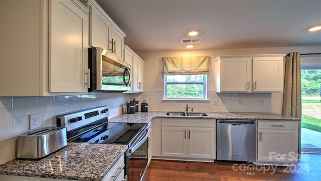 kitchen featuring appliances with stainless steel finishes, a wealth of natural light, dark wood-type flooring, and light stone counters