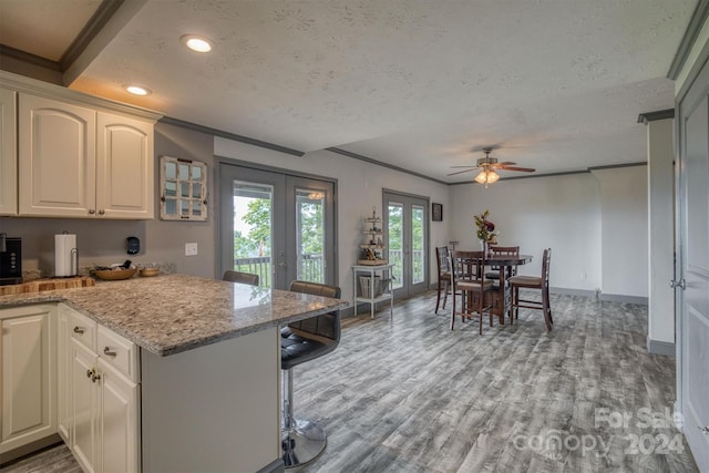 kitchen featuring kitchen peninsula, white cabinetry, light stone counters, a textured ceiling, and ornamental molding