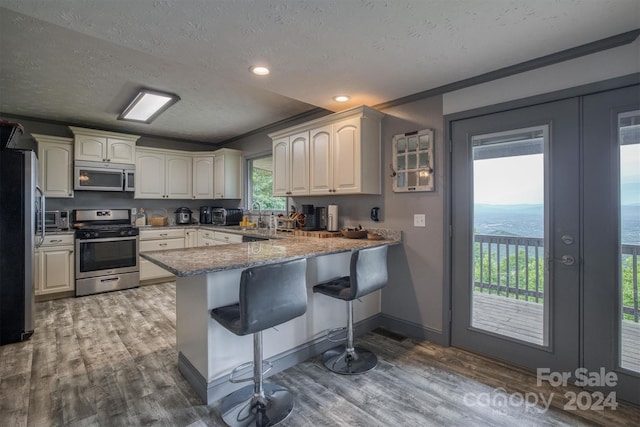 kitchen featuring kitchen peninsula, appliances with stainless steel finishes, a water view, a textured ceiling, and a breakfast bar area