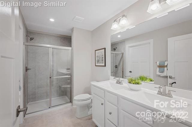 bathroom with vanity with extensive cabinet space, toilet, tile floors, a shower with door, and double sink