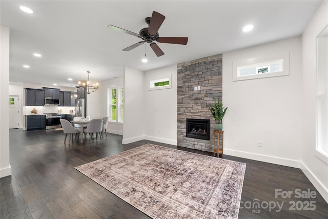 living room featuring ceiling fan with notable chandelier, a fireplace, and dark wood-type flooring