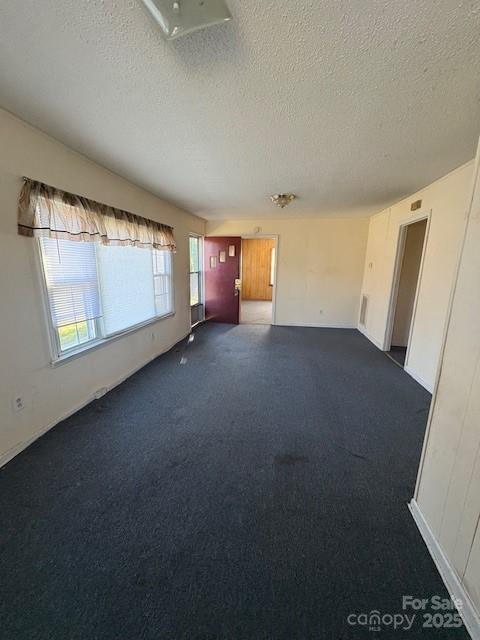 unfurnished living room featuring dark carpet and a textured ceiling