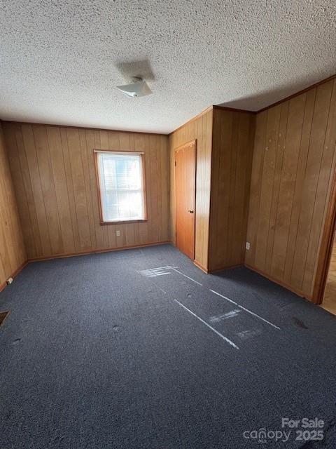 unfurnished bedroom with wooden walls, a closet, a textured ceiling, and dark colored carpet