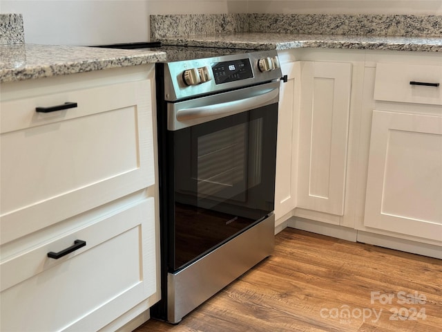 room details with white cabinets, light stone countertops, stainless steel range with electric cooktop, and light wood-type flooring