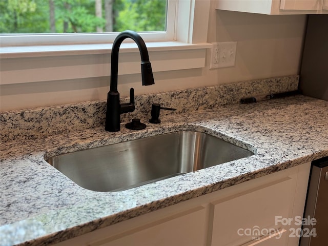 interior details featuring white cabinets, light stone counters, and sink