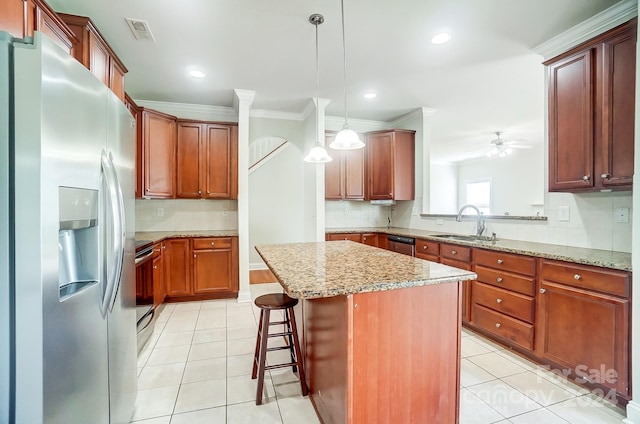 kitchen with hanging light fixtures, light tile patterned floors, appliances with stainless steel finishes, a kitchen island, and light stone countertops