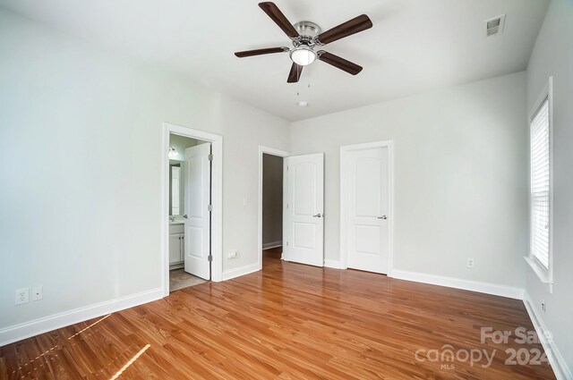 unfurnished bedroom with hardwood / wood-style flooring, ceiling fan, connected bathroom, and multiple windows