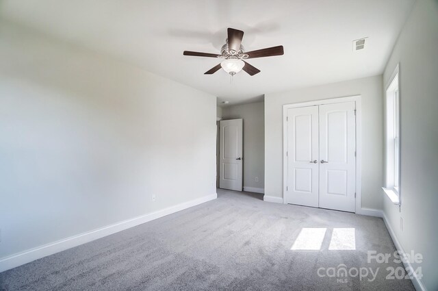 unfurnished bedroom with multiple windows, a closet, ceiling fan, and light carpet