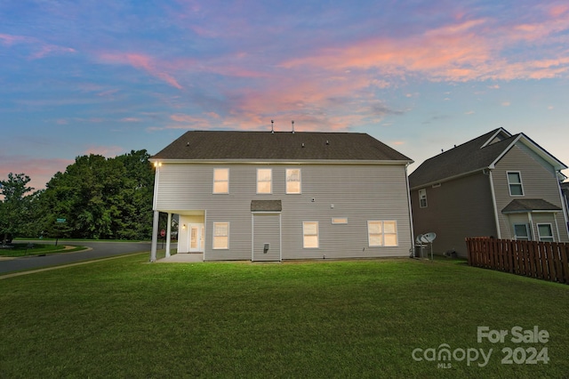 back house at dusk featuring a patio area and a lawn