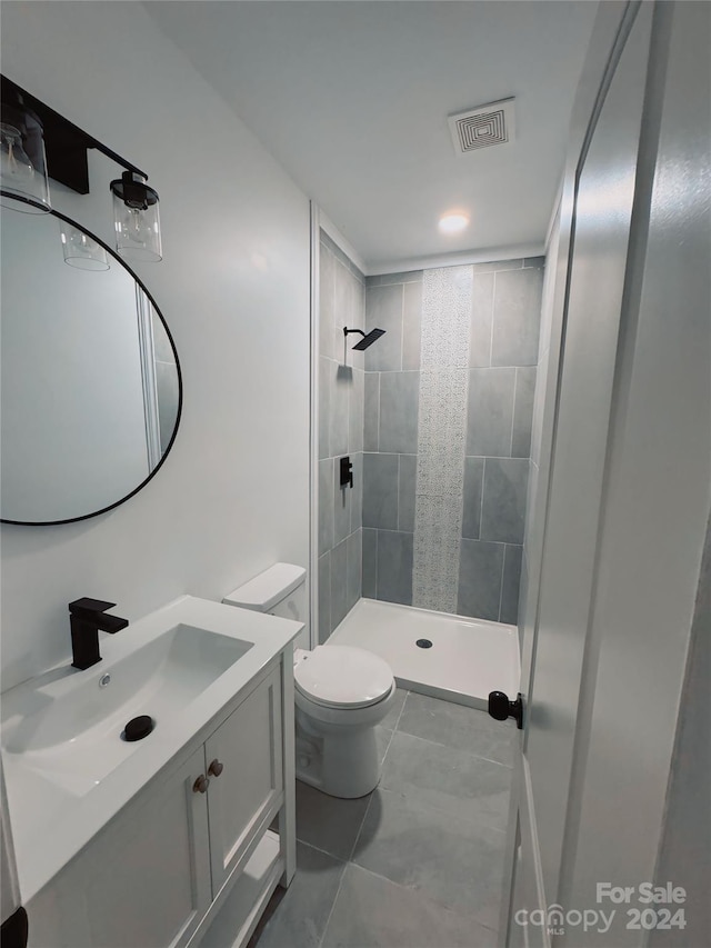 bathroom with tile patterned flooring, toilet, a tile shower, and vanity