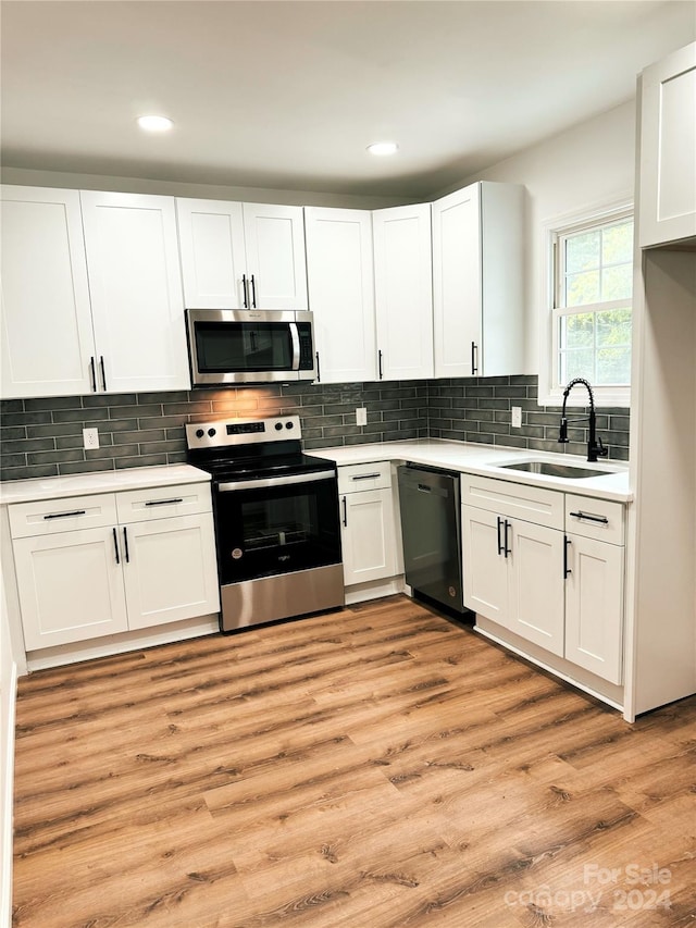 kitchen with white cabinetry, sink, stainless steel appliances, tasteful backsplash, and light hardwood / wood-style flooring