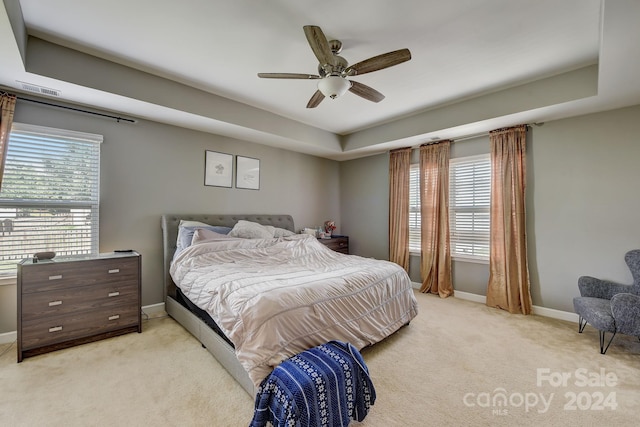 bedroom with light carpet, a raised ceiling, and ceiling fan