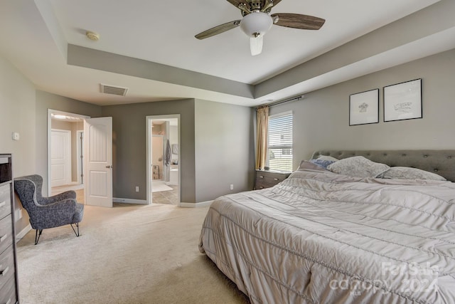 carpeted bedroom with a raised ceiling, ensuite bath, and ceiling fan