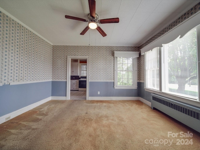 spare room featuring light carpet, radiator, ceiling fan, and crown molding