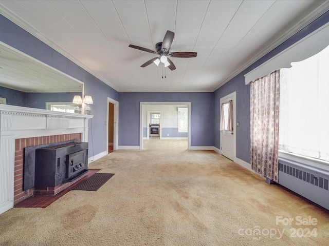 unfurnished living room with carpet, radiator heating unit, a wood stove, ornamental molding, and ceiling fan