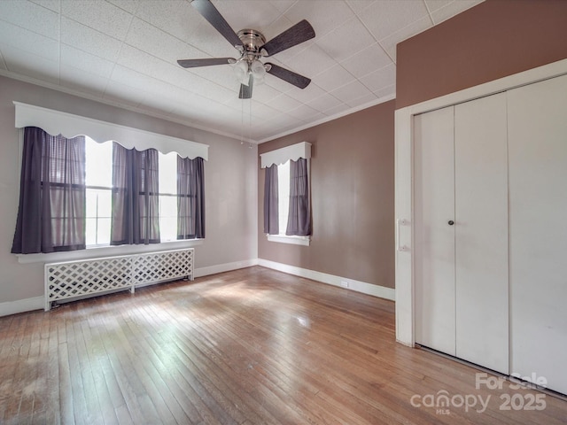 unfurnished bedroom with radiator, hardwood / wood-style flooring, ceiling fan, crown molding, and a closet