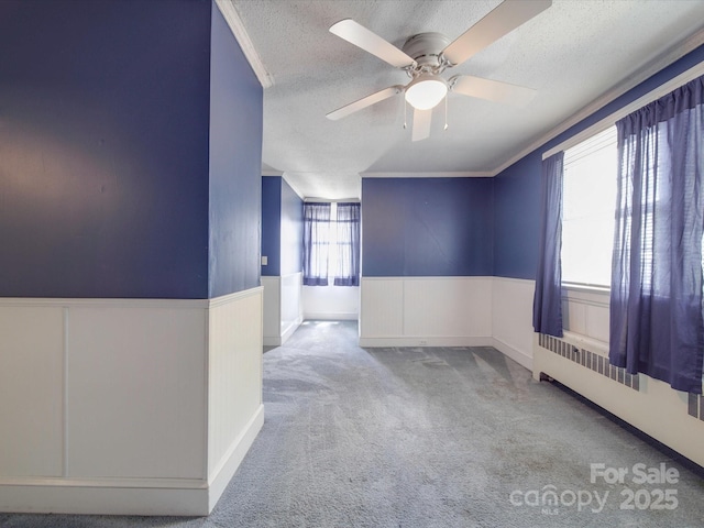 carpeted empty room with ceiling fan, ornamental molding, and a textured ceiling