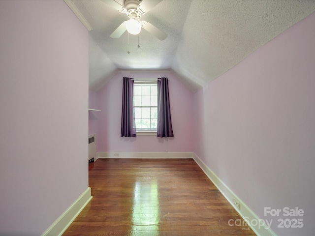 additional living space featuring ceiling fan, hardwood / wood-style floors, radiator heating unit, a textured ceiling, and vaulted ceiling