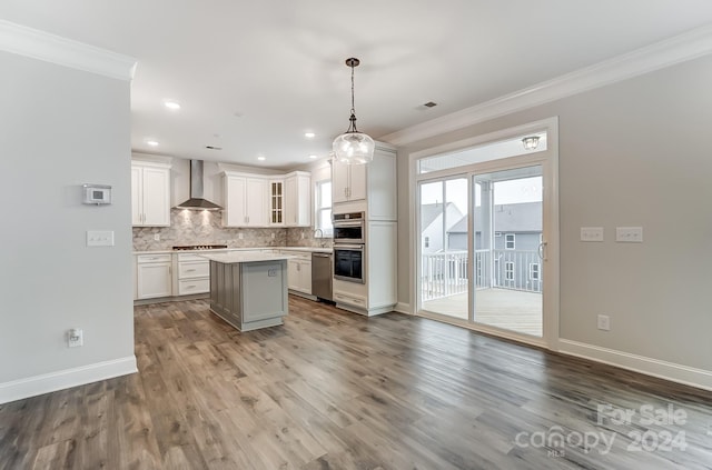 kitchen featuring wall chimney exhaust hood, stainless steel appliances, white cabinets, a center island, and hanging light fixtures