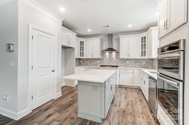 kitchen featuring wall chimney exhaust hood, a kitchen island, light hardwood / wood-style floors, white cabinets, and appliances with stainless steel finishes