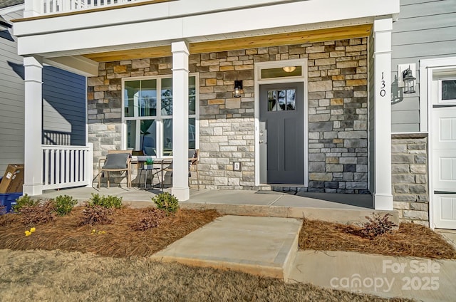 view of exterior entry with stone siding and a porch