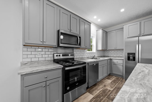 kitchen with appliances with stainless steel finishes, gray cabinetry, backsplash, dark hardwood / wood-style flooring, and light stone countertops