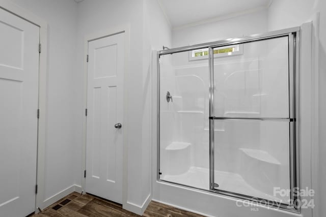 bathroom with hardwood / wood-style flooring, a shower with shower door, and crown molding