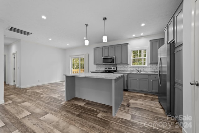 kitchen with hanging light fixtures, a kitchen island, gray cabinets, stainless steel appliances, and hardwood / wood-style floors