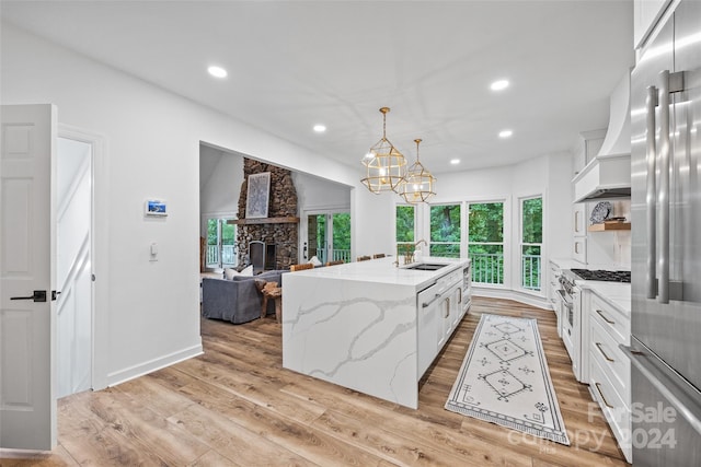 kitchen featuring hanging light fixtures, light stone countertops, a kitchen island with sink, and white cabinets