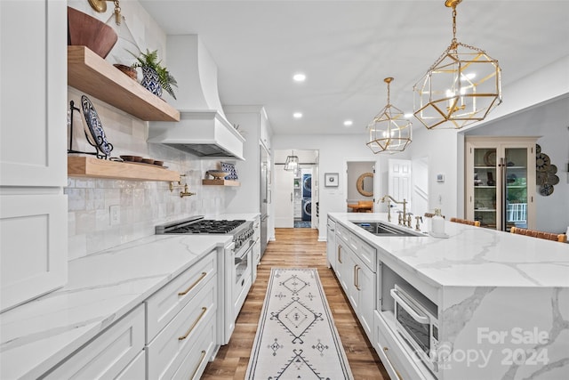 kitchen featuring custom exhaust hood, a center island with sink, hanging light fixtures, appliances with stainless steel finishes, and white cabinets