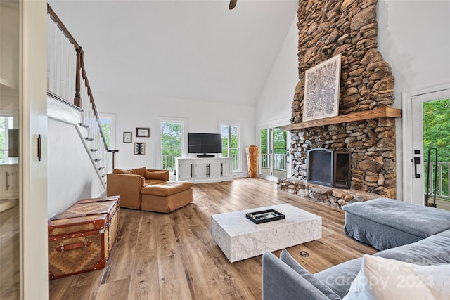 living room with a stone fireplace, high vaulted ceiling, and light wood-type flooring