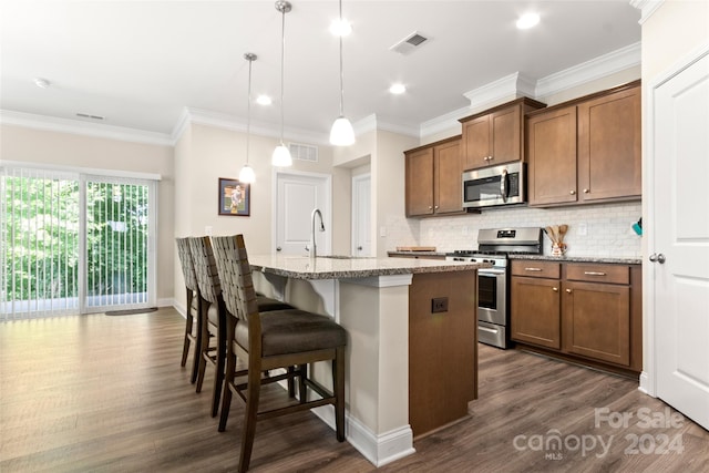 kitchen featuring appliances with stainless steel finishes, dark wood-type flooring, a center island with sink, and pendant lighting