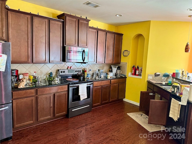 kitchen featuring decorative backsplash, dark stone countertops, appliances with stainless steel finishes, decorative light fixtures, and dark hardwood / wood-style flooring