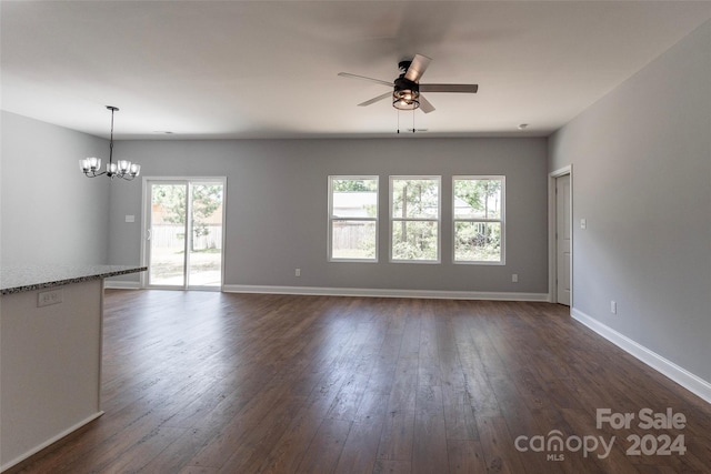 empty room featuring ceiling fan with notable chandelier, a wealth of natural light, and dark wood-type flooring