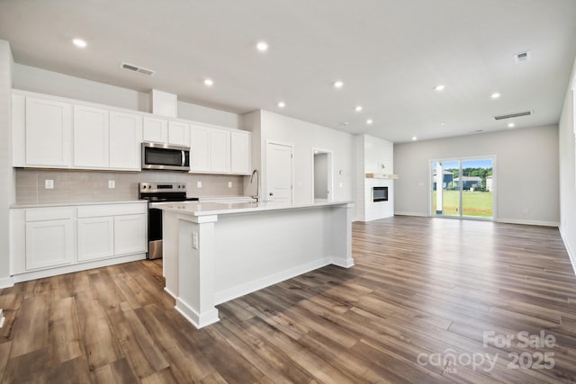 kitchen with decorative backsplash, appliances with stainless steel finishes, dark hardwood / wood-style flooring, white cabinets, and an island with sink