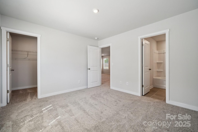 unfurnished bedroom with light carpet, a walk in closet, ensuite bath, and a closet