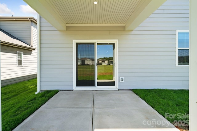 view of exterior entry with a lawn and a patio