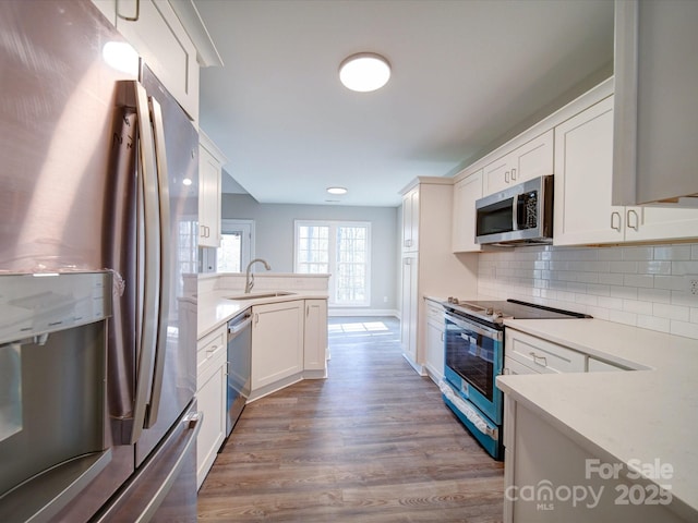 kitchen with hardwood / wood-style floors, decorative backsplash, white cabinetry, appliances with stainless steel finishes, and sink